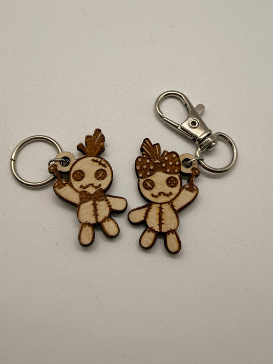 Two wooden keychains shaped like voodoo dolls on a light gray background