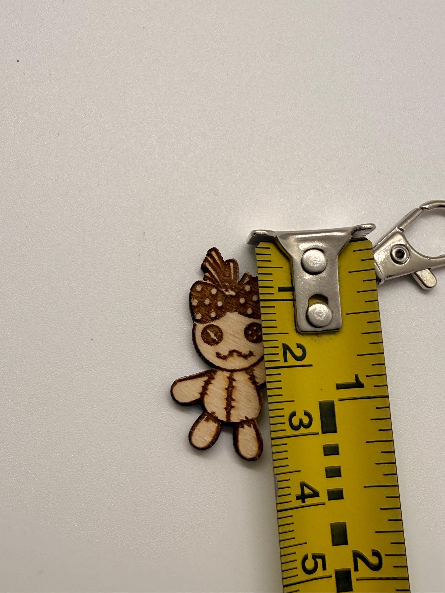 Wooden voodoo doll-shaped keychain with a measuring tape for scale on a white background