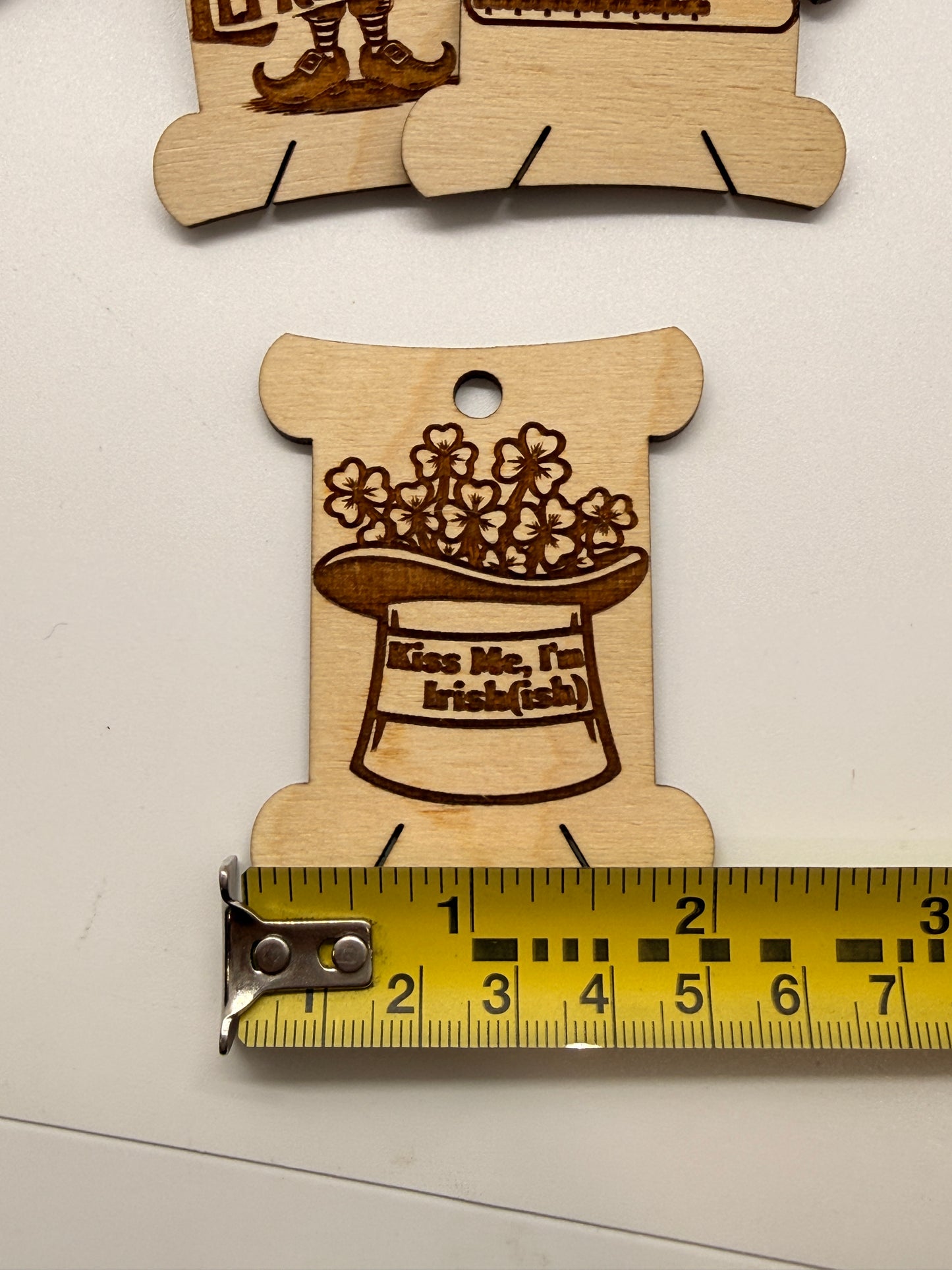 Wooden cutout with laser engraving of a hat and flowers, next to a ruler for scale.