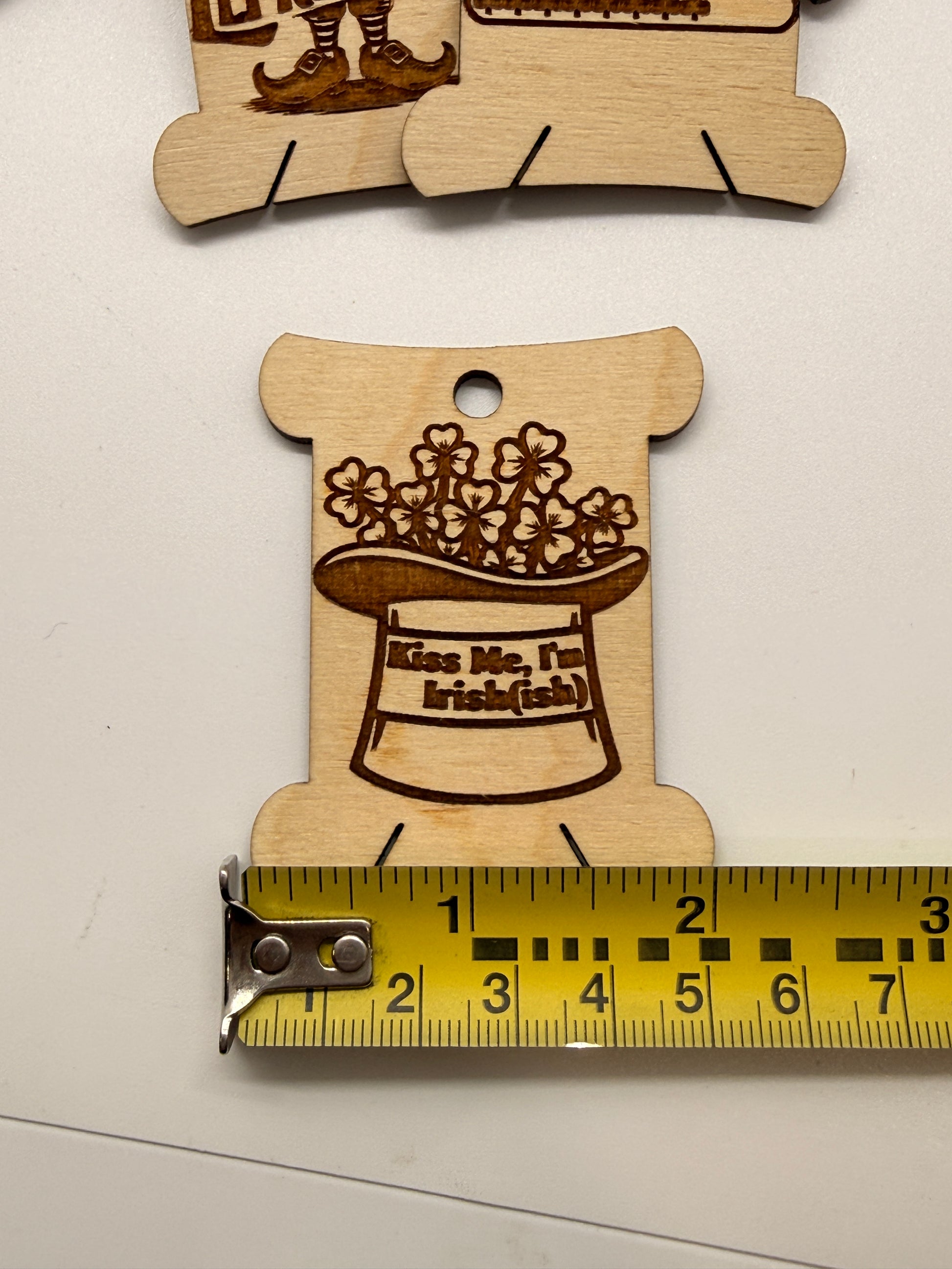 Wooden cutout with laser engraving of a hat and flowers, next to a ruler for scale.