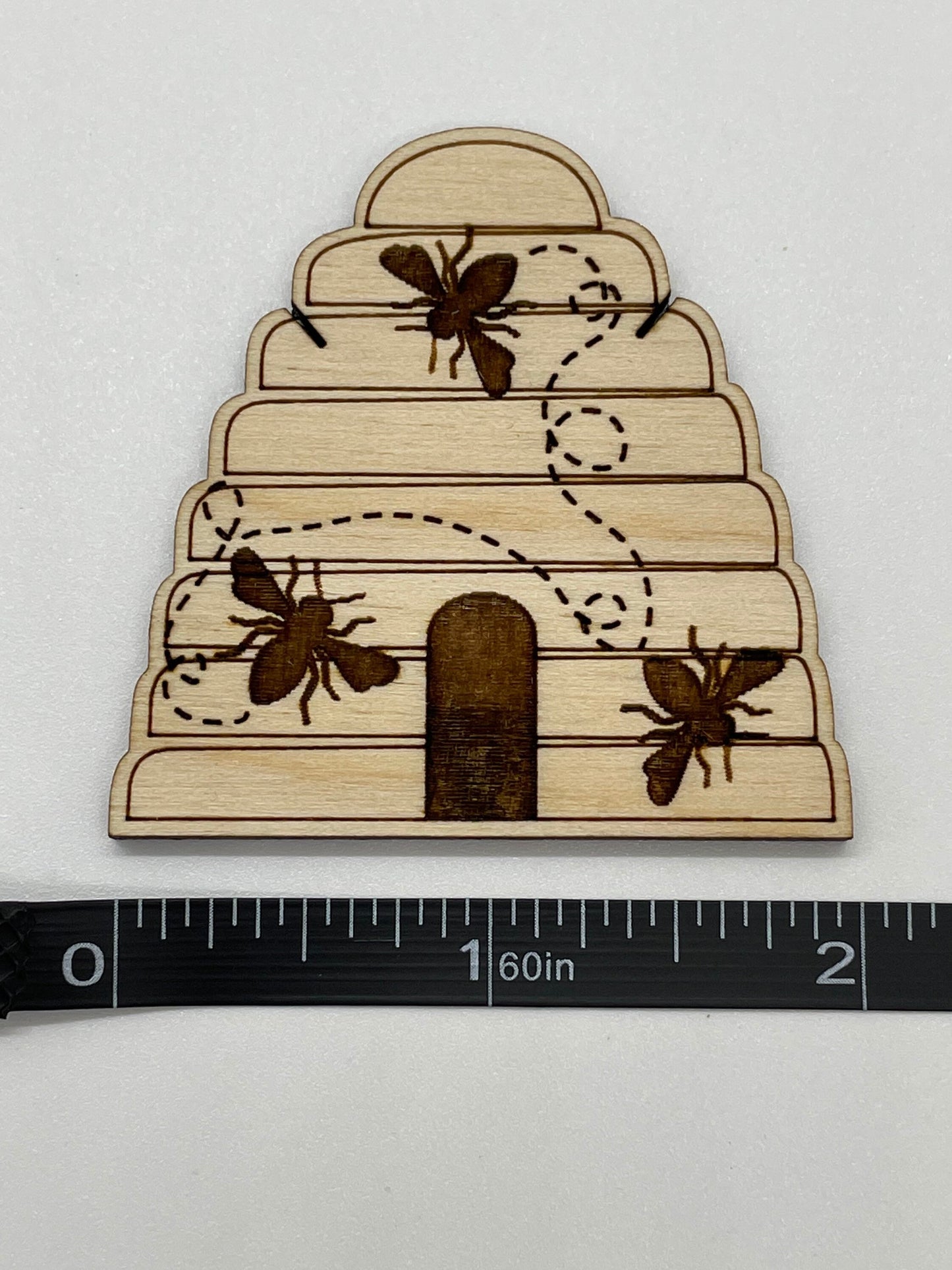 Wooden beehive model with bees and honeycomb pattern on a white background, measured against a ruler.
