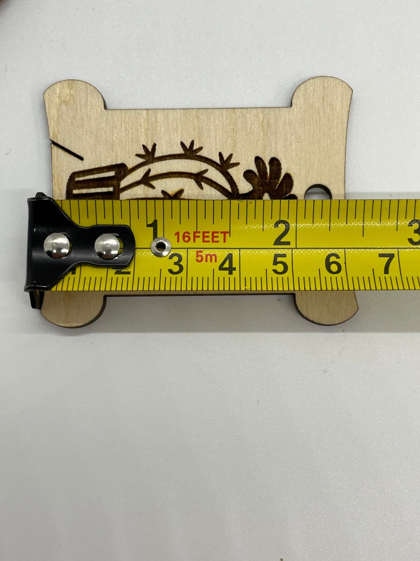 Wooden decorative item with laser cut design on a white background, measured by a tape measure.