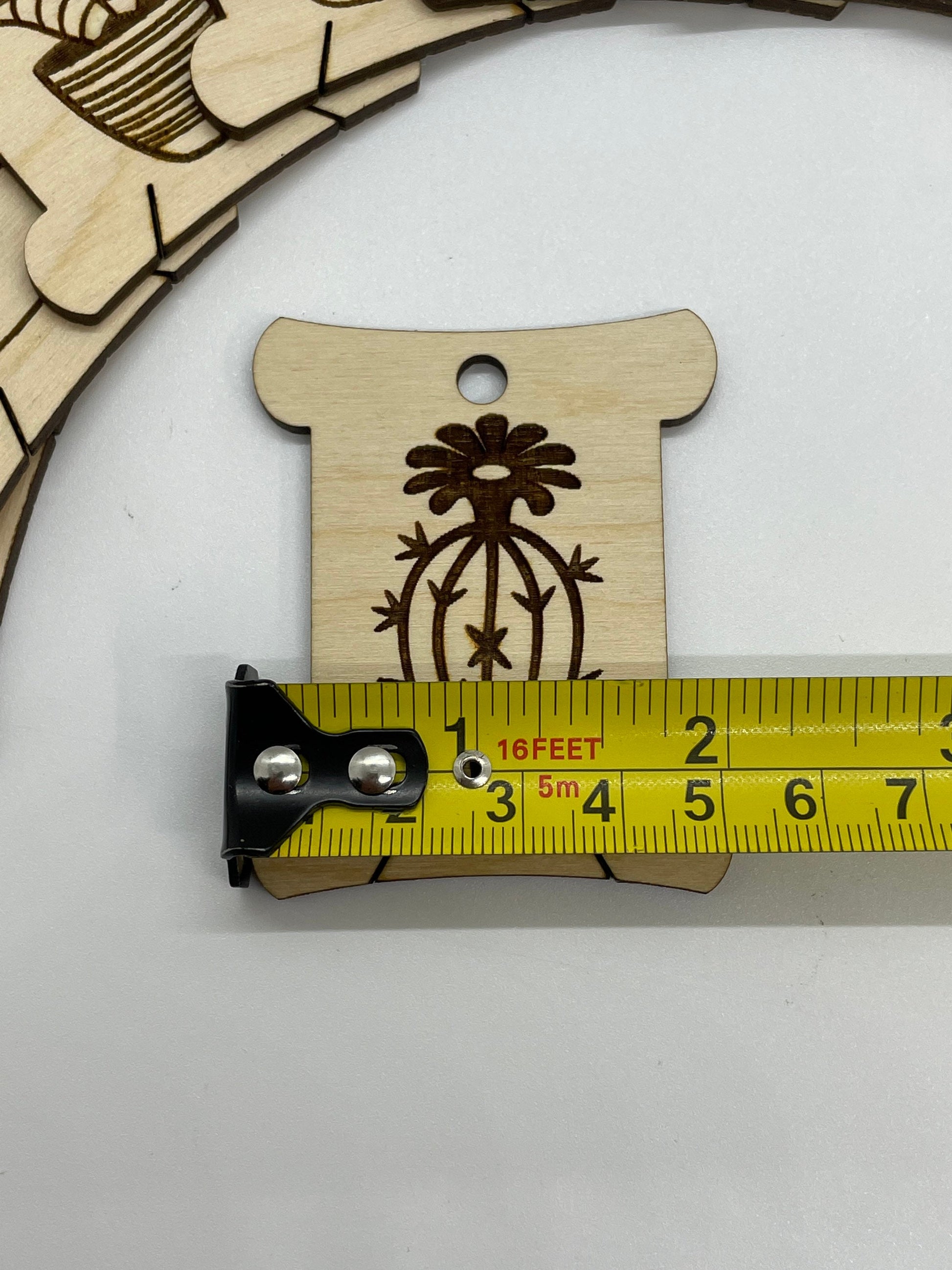 Wooden pendant with floral design next to a measuring tape on a white background