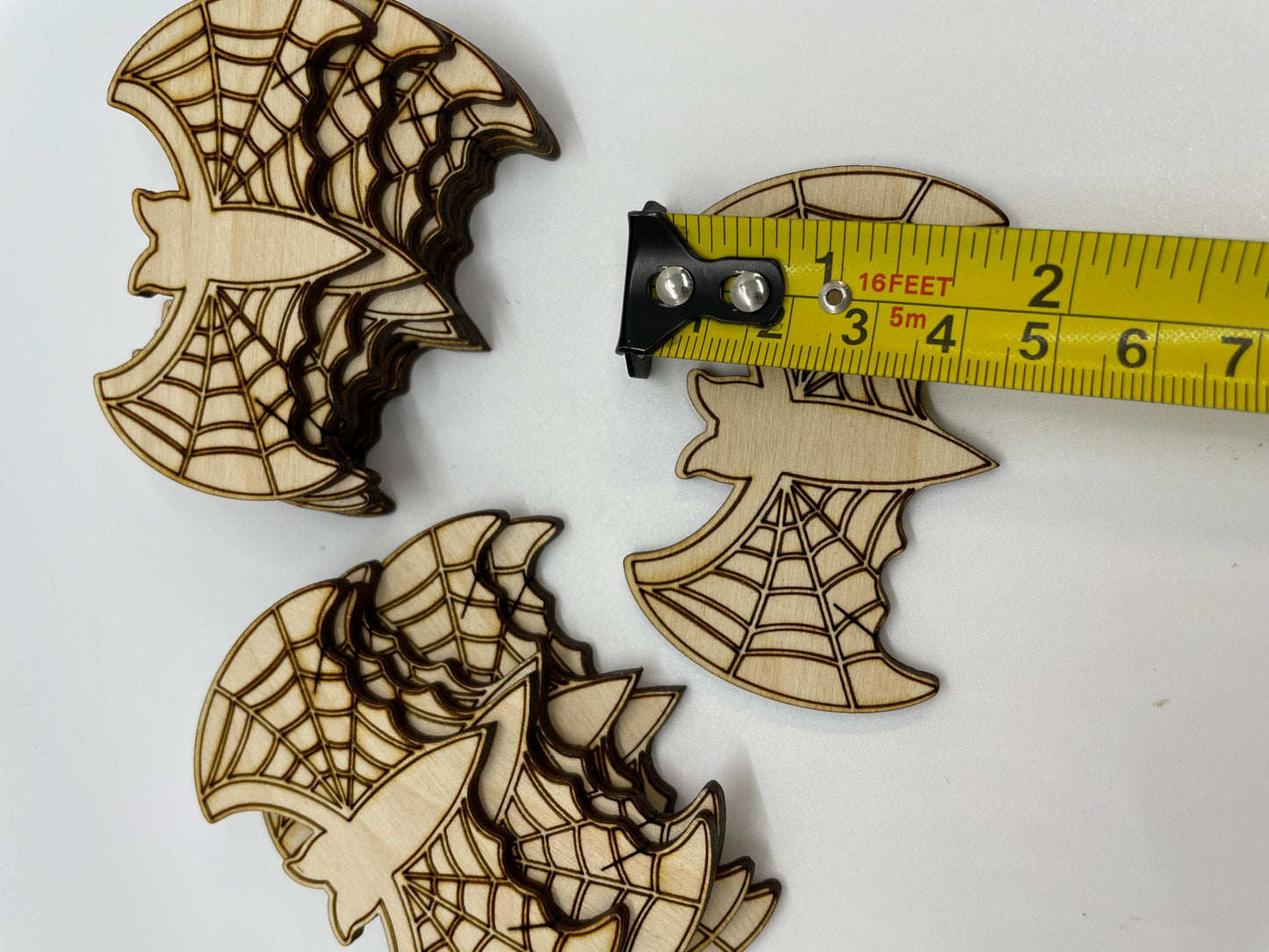 Wooden cutouts with spider web design and measuring tape for scale on a white background