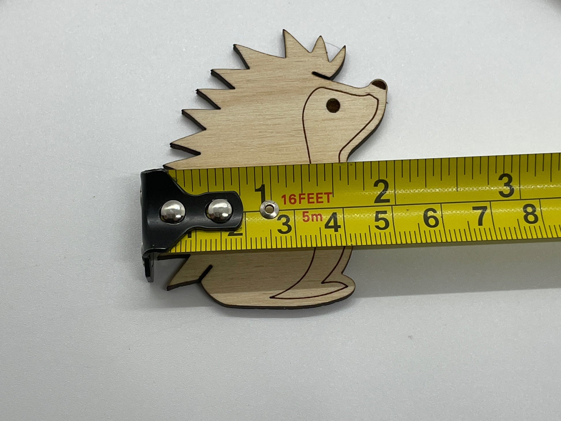 Wooden hedgehog-shaped bobbin with a measuring tape for scale on a white background