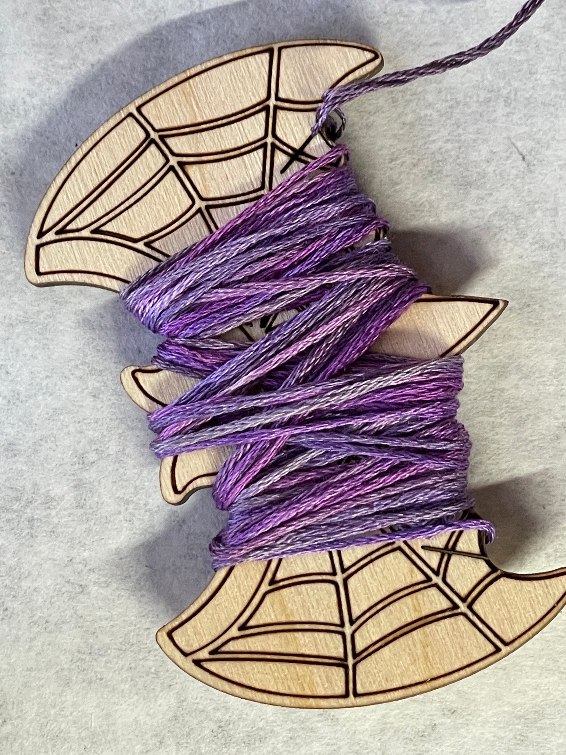 Two skeins of purple yarn on a wooden spider web design