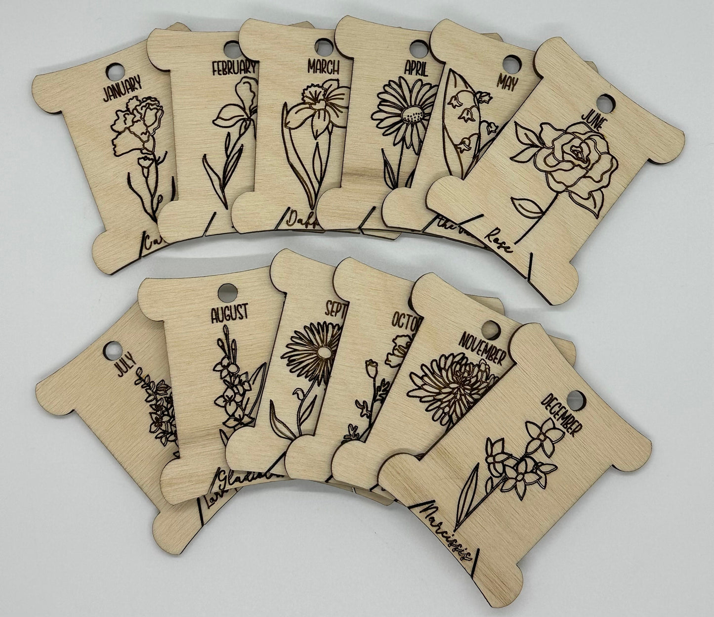 Wooden bobbins with floral designs and months of the year text on a light gray background