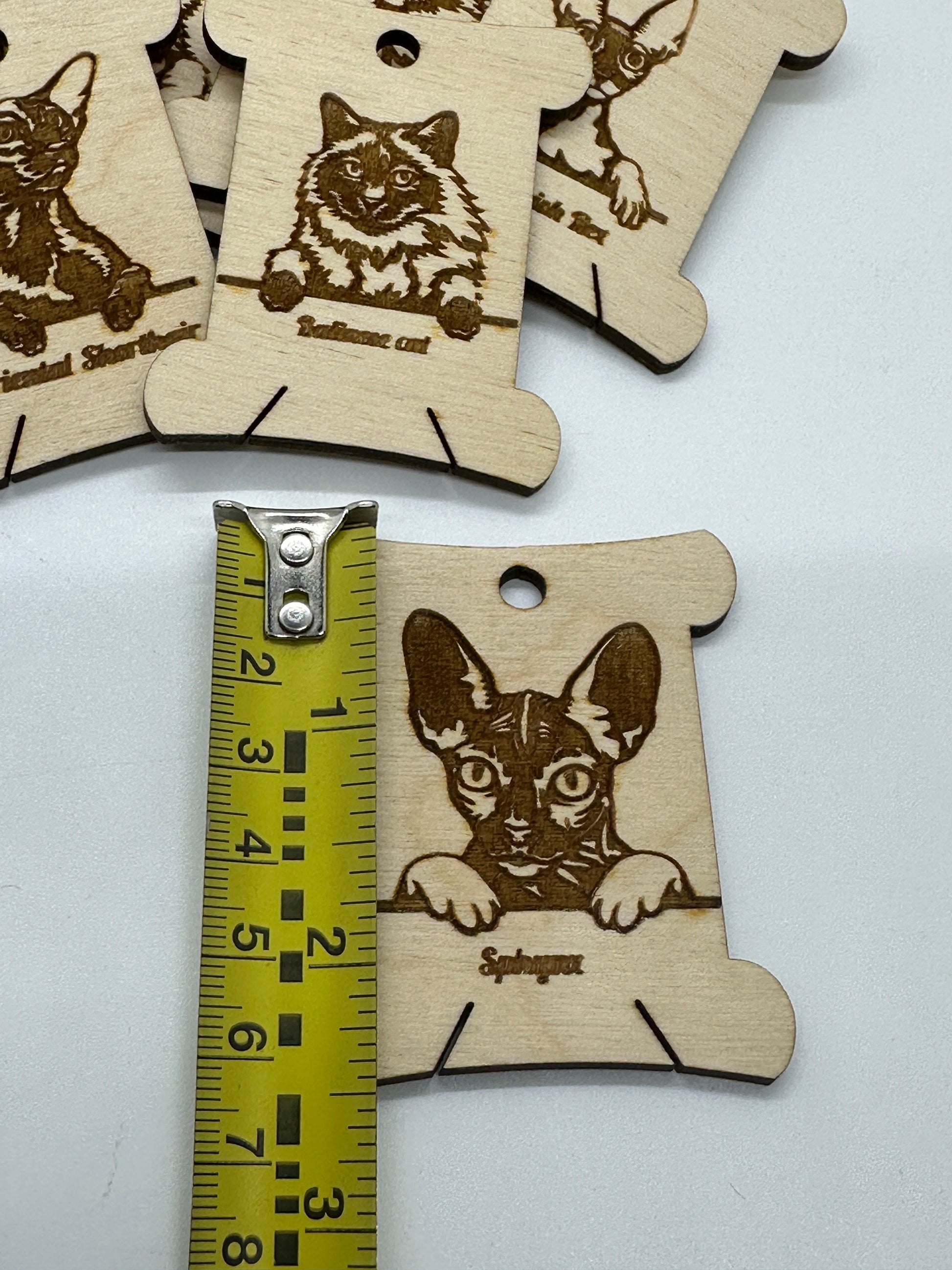 Wooden dog tags with engraved cat designs and a ruler for scale on a white background