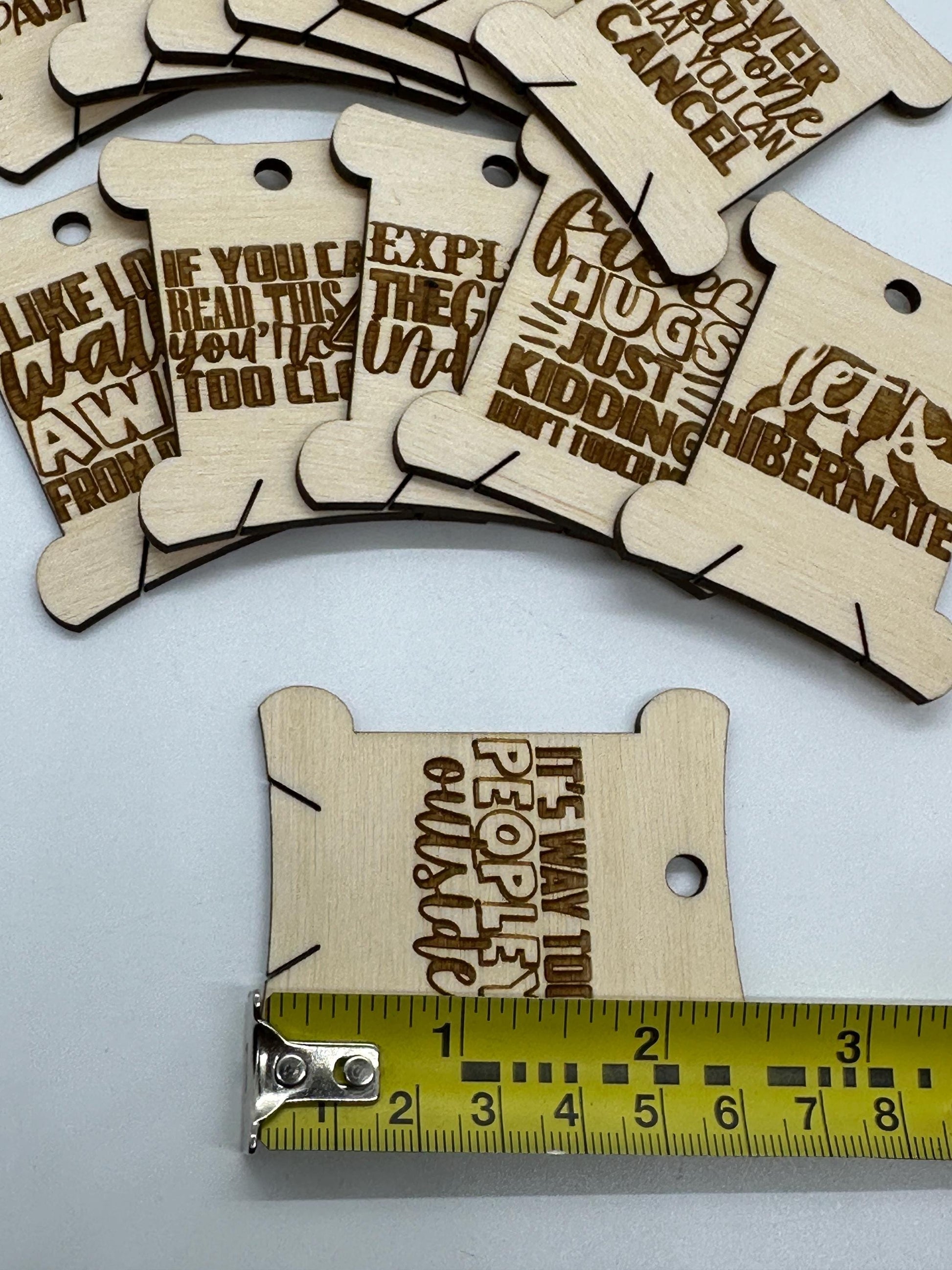 Wooden tags with laser-cut text on a white background, with a ruler for scale.