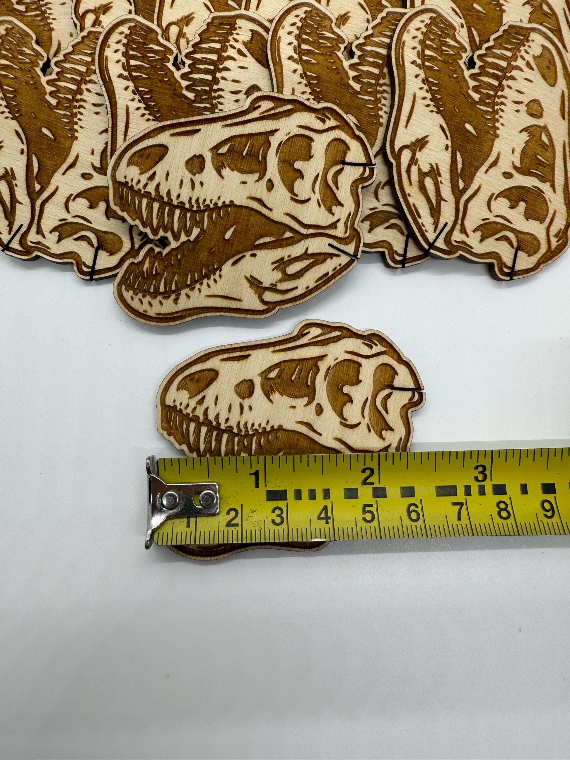 Dinosaur skull-shaped wooden cutouts with a measuring tape for scale on a white background