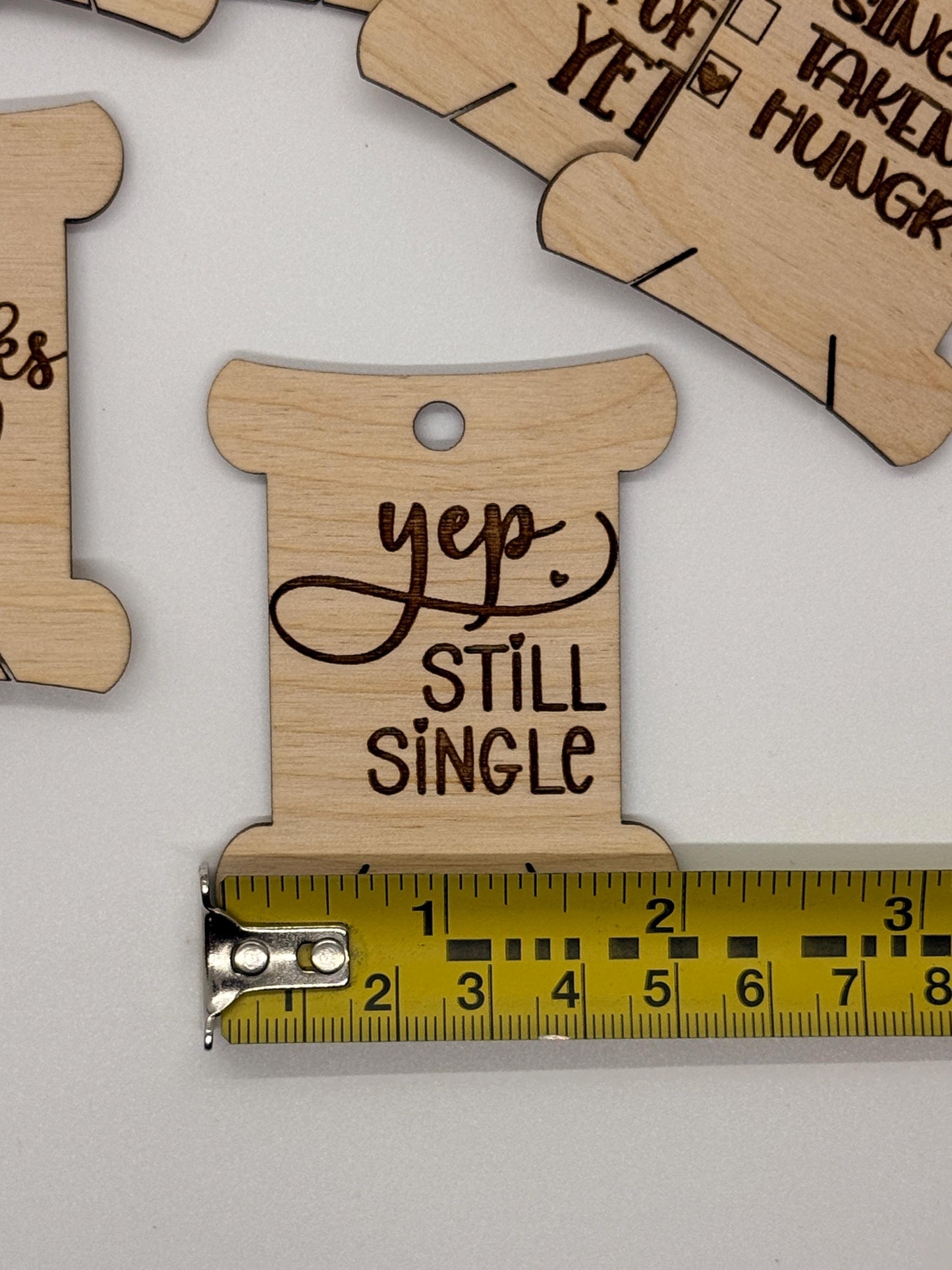 Wooden sign with 'Yep, Still Single' text and a tape measure for scale on a white background.