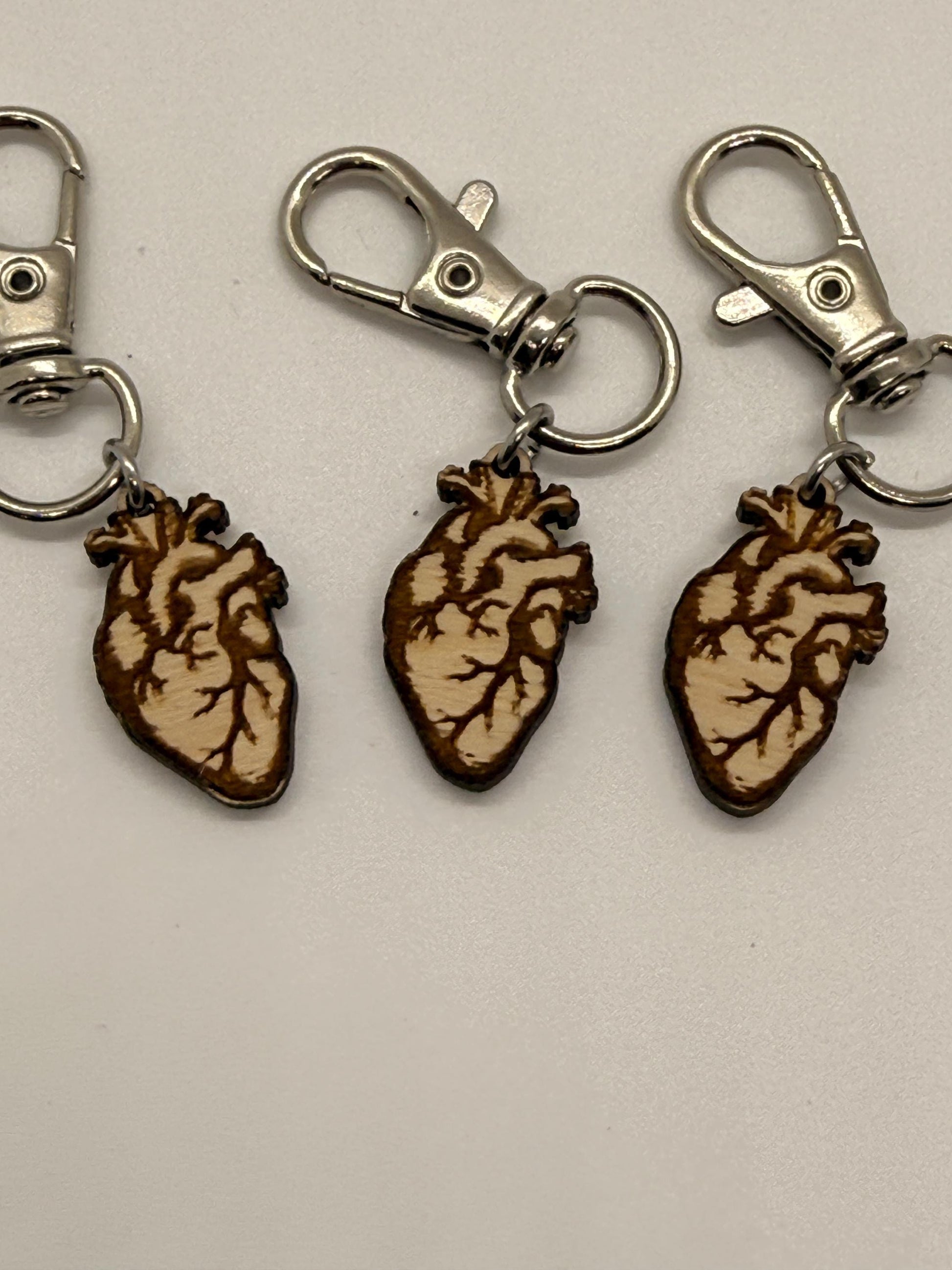 Three keychains with anatomical heart designs on a light gray background