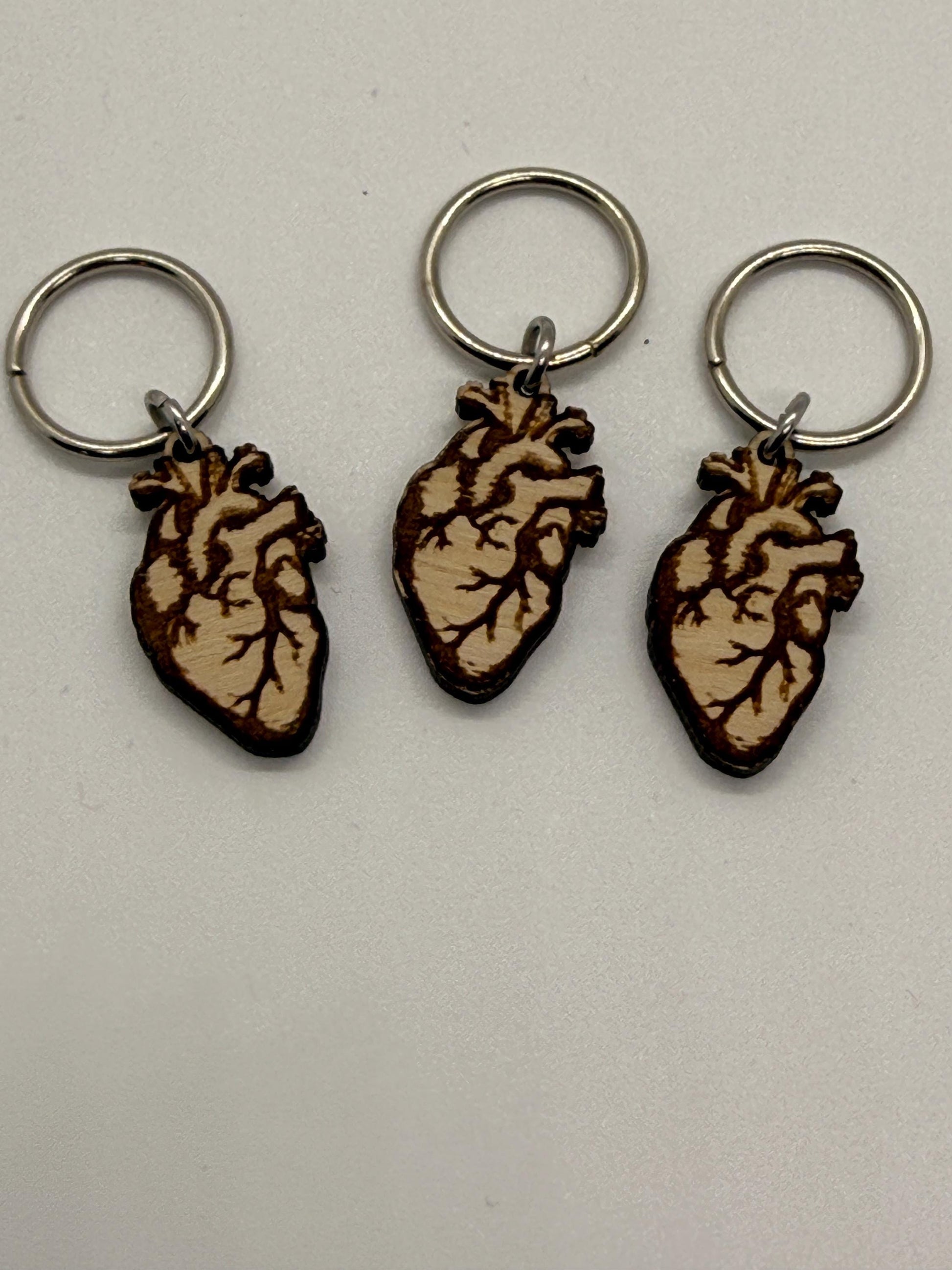 Three wooden heart-shaped keychains with metal rings on a light gray background